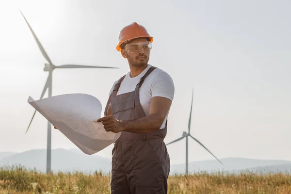 Technician standing of windmill farm with blueprints — 图库照片