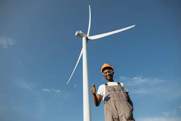 Engineer in uniform gesturing with fingers thumbs up at windmill farm — Zdjęcie stockowe