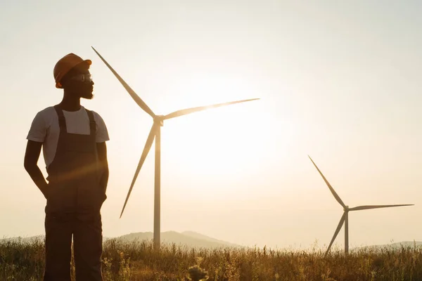 Inżynier stojący na polu z wiatrakami podczas zachodu słońca — Zdjęcie stockowe