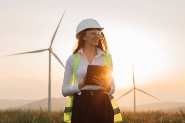 Yenilenebilir enerji çiftliğinde tabletle çalışan kasklı kadın.
