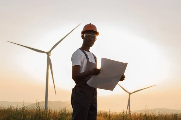 Engineer with blueprints standing among windmill farm — Zdjęcie stockowe