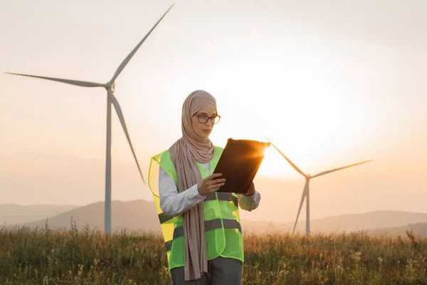 Woman in hijab standing on windmill farm with clipboard — Zdjęcie stockowe