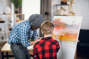 Son and father using brush and paints for drawing