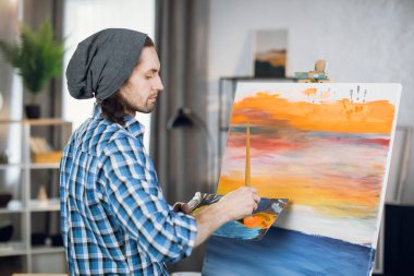 Man painting on canvas with brush and color palette