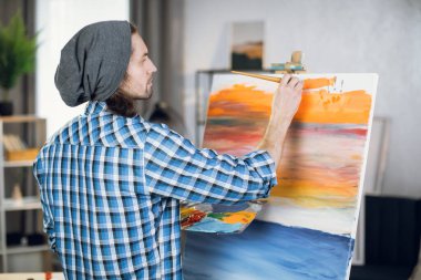Man standing in front of easel and painting with brush