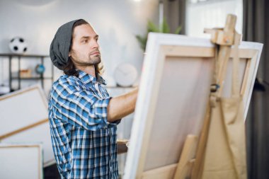 Man in casual wear painting on easel in studio