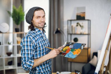 Man posing at art studio with brush and color palette