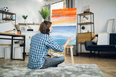 Artist in headset listening music and drawing on canvas