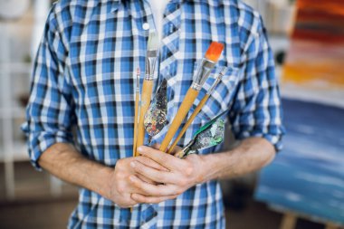 Male artist holding brushes and spatula in hands