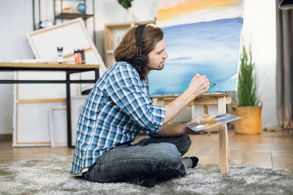 Man in headphones listening music and painting on easel — Φωτογραφία Αρχείου