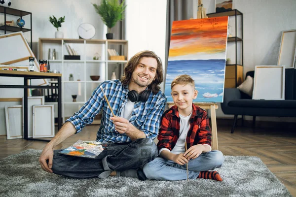 Father and son sitting on floor near colorful easel — Foto de Stock