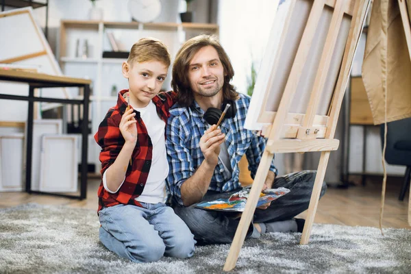 Son embracing father while painting together on canvas — Foto de Stock