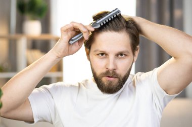 Close-up of a young positive caucasian guy in a white t-shirt combing his hair