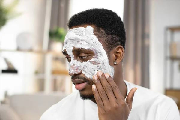 African american guy applying white facial mask on face and looking on camera — Stock Photo, Image