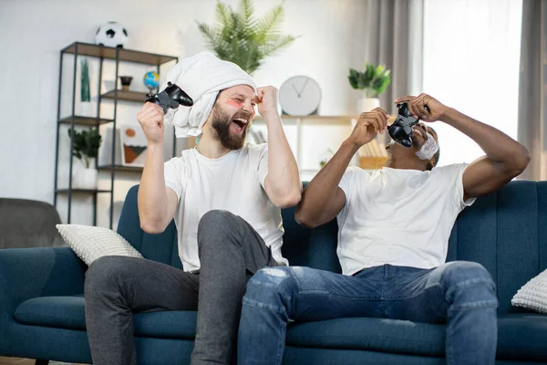 Multiethnic men doing skin care procedures, playing video games using joysticks