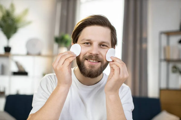 Bearded guy smiling at camera and having fun while playing with cotton pads, covering his eye — Stock Photo, Image