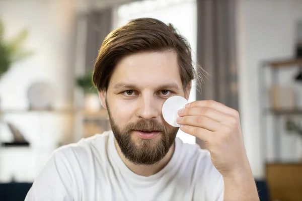 Handsome smiling bearded young caucasian guy posing to camera and presenting cotton pads — Stock Photo, Image