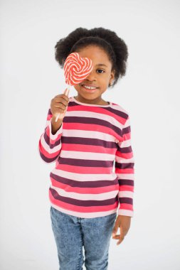 Bir gözünü renkli lolipopun altına saklayan tatlı küçük çocuk.