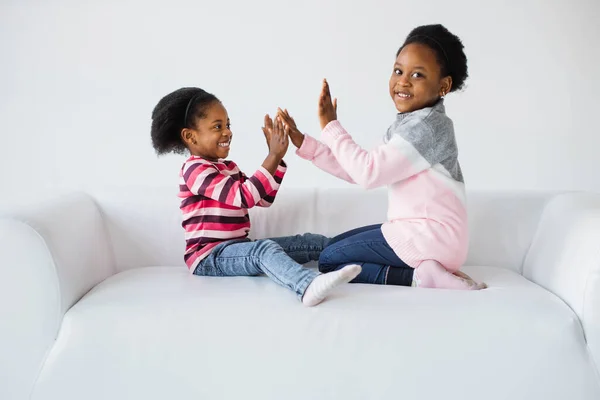 Two pretty african sisters playing together on white sofa — Stock Photo, Image