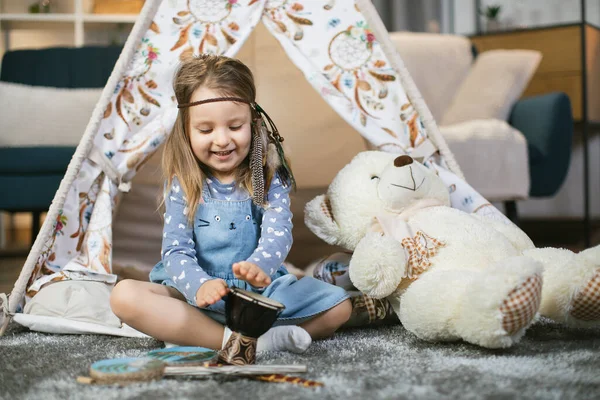 Wigwam 'da otururken küçük bir davul çalan dişi çocuk. — Stok fotoğraf