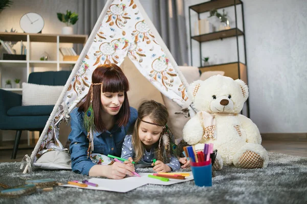 Anne ve kızı evdeki oyuncak çadırın yakınına resim çiziyor. — Stok fotoğraf