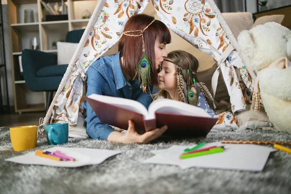 Zorgzame moeder zoenen dochter tijdens storytelling thuis — Stockfoto