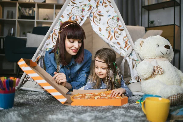 Moeder en dochter eten pizza in speelgoed wigwam — Stockfoto
