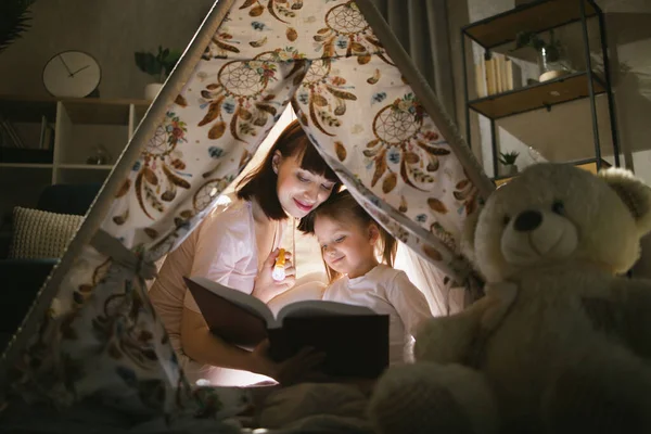 Vrouw lezen boek aan dochter binnen tipi in donkere kamer — Stockfoto