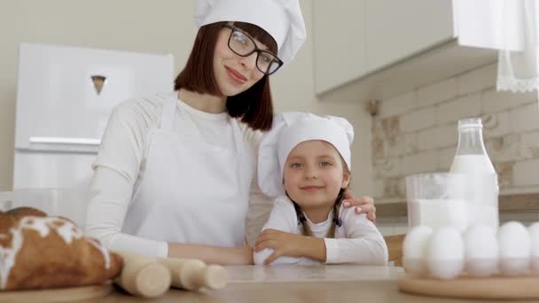 Amistosa madre joven abraza a su hija pequeña mientras cocina la panadería de postres en la cocina moderna — Vídeos de Stock