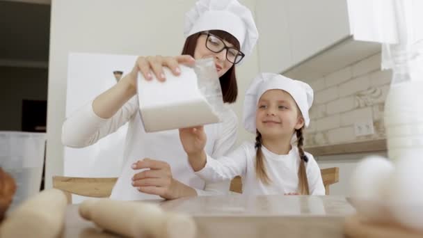 Madre e hija niña niña vertiendo harina en el tablero de plástico para galletas y divertirse en la cocina. — Vídeos de Stock