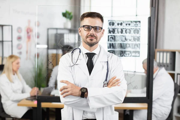Medico caucasico uomo in occhiali posa con le braccia incrociate — Foto Stock
