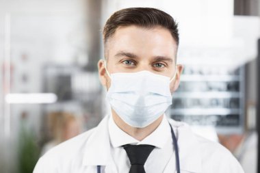 İş yerinde poz veren maskeli doktor ve laboratuvar önlüğü.