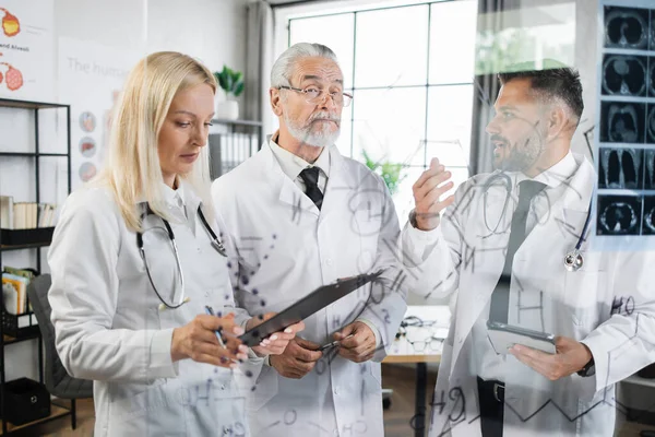 Médecins écrivant sur tableau à feuilles mobiles tout en examinant le balayage par rayons X — Photo