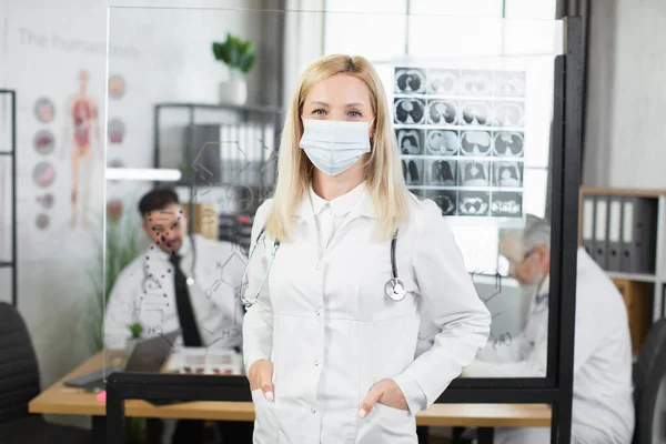 Жінка-лікар в масці для обличчя і лабораторне пальто позує в приміщенні — стокове фото