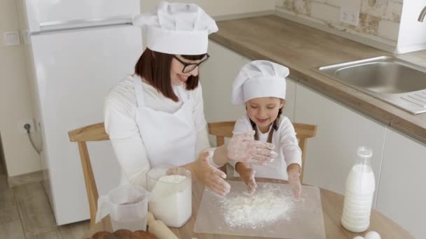 Adorável menina e sua mãe branca em chapéus de chef batendo palmas com farinha — Vídeo de Stock
