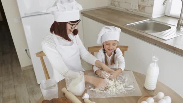 Linda chica y su hermosa mamá en sombreros de chef y delantal para cocinar se miran entre sí — Vídeos de Stock