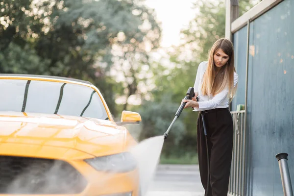 Başarılı iş kadını beyaz gömlek ve siyah pantolon giyiyor, sarı arabasını yıkıyor. — Stok fotoğraf