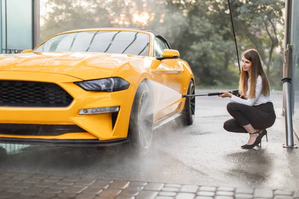 Gambar horisontal wanita bisnis mengenakan kemeja dan celana panjang, mencuci roda mobil kuning nya — Stok Foto