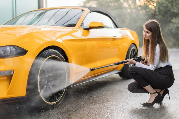 Горизонтальний знімок ділової жінки, що носить сорочку та штани, миє жовте колесо автомобіля — стокове фото