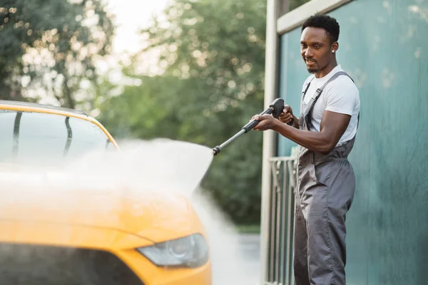 Hombre joven africano guapo en mono protector, lavando su coche amarillo —  Fotos de Stock