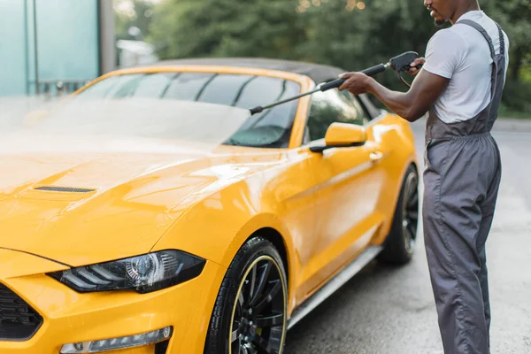 Gri tulumlu, beyaz tişörtlü, sarı lüks araba yıkayan Afrikalı adam. — Stok fotoğraf