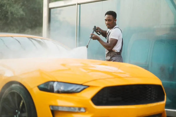 Mężczyzna myje swój luksusowy żółty samochód pod wysokim ciśnieniem strumieniem wody na zewnątrz w myjni samoobsługowej. — Zdjęcie stockowe