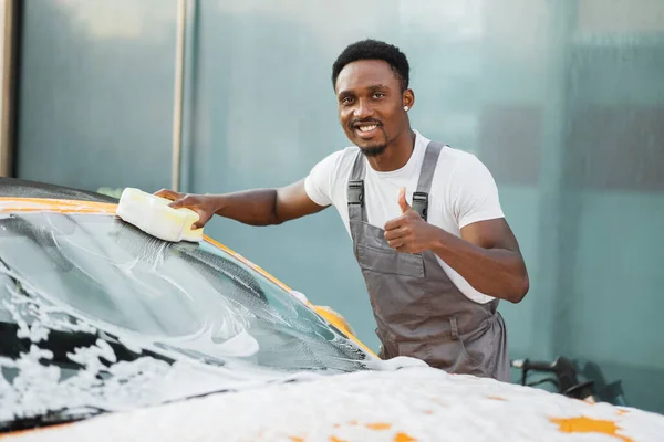 Joven atractivo hombre afroamericano lavando su coche con espuma limpiadora y esponja amarilla. — Foto de Stock