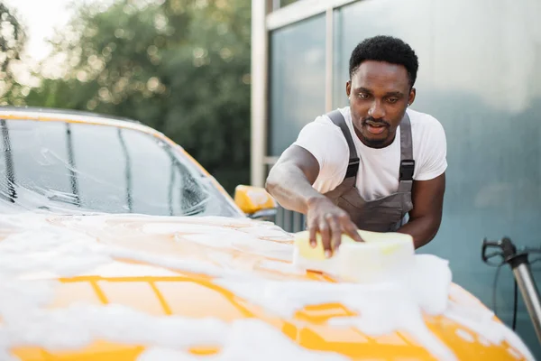 Çekici Afrikalı genç adam modern lüks arabasını oto yıkama istasyonunda yıkıyor. — Stok fotoğraf
