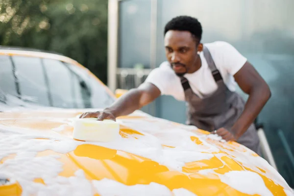 Afrikalı adam kameraya bakıyor ve arabayı yıkarken mutlu bir gülümsemeyle baş parmağını kaldırıyor. — Stok fotoğraf