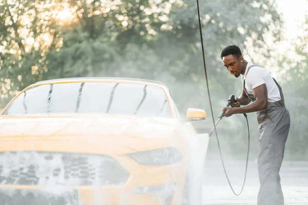 Afroamerykanin myje samochód pod wysokim ciśnieniem strumieniem wody na zewnątrz — Zdjęcie stockowe