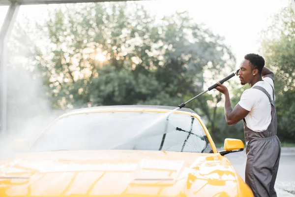 Yakışıklı adam lüks sarı arabasını yüksek basınçlı su pompasıyla yıkıyor. — Stok fotoğraf