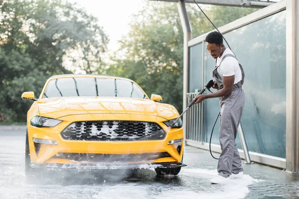 Pria mencuci mobil kuning mewahnya di bawah tekanan tinggi air jet — Stok Foto