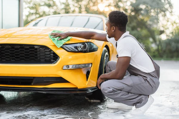 Pemuda Afrika mencuci dan menyeka modern olahraga kap mobil kuning — Stok Foto