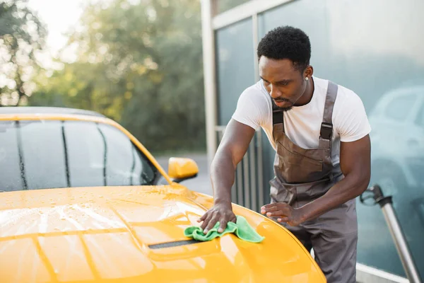 Lövés jóképű szakállas fiatal afrikai srác munkás takarítás sárga autó motorháztető — Stock Fotó